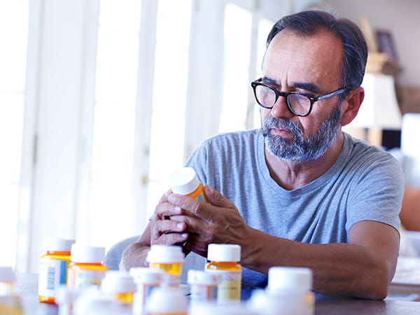 Un hombre de origen latino de edad avanzada está sentado y ordena unos medicamentos con receta en una mesa.